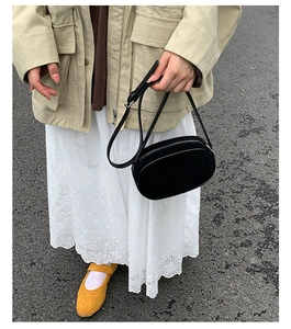 Outdoor street style model holding a black oval crossbody bag with silver zipper detail