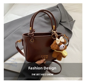 Détail d'un mini sac seau en cuir marron foncé avec charm ours et logo en métal