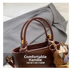 Détail du sac seau en cuir marron foncé avec poignée nouée et breloque ourson