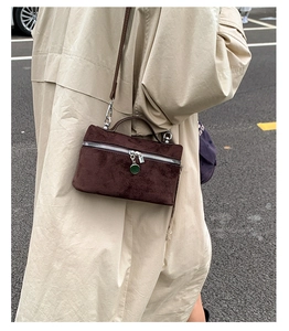 Detail of a dark brown suede crossbody mini bag with a green enamel pendant charm