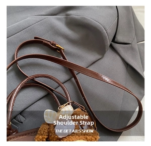 Détail de la bandoulière réglable en cuir avec boucle dorée et pendentif ours en peluche