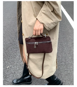 Detail of dark brown suede crossbody bag with silver hardware on a street background