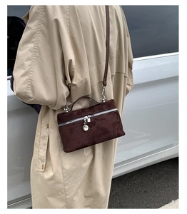 Detail of dark brown suede handbag with silver hardware worn with a beige trench coat