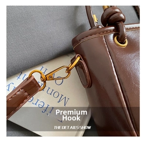 Détail d'un sac seau en cuir marron montrant le fermoir pivotant en métal doré et coutures