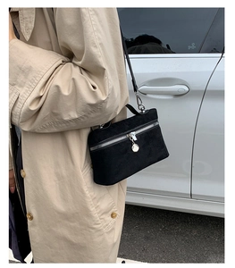 Detail of black suede crossbody bag with silver chain and zipper on trench coat