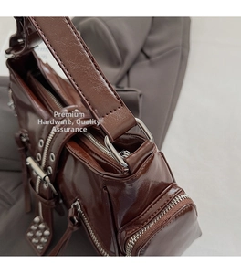 Detail of dark brown glossy leather shoulder bag with silver hardware and zippers