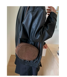 Detail view of a dark brown suede crossbody bag worn by a model in an indoor setting