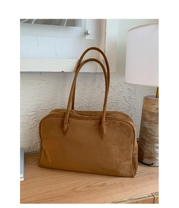 Detalle de bolso Boston de ante marrón sobre mesa de madera con lámpara minimalista