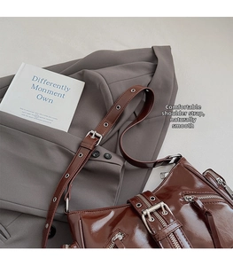 Close-up of dark brown glossy underarm bag with zipper details and metallic eyelets