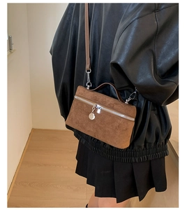Brown suede crossbody bag with silver hardware on a model wearing a black jacket