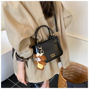 Détail d'un sac seau en cuir noir brillant avec garniture dorée et pendentif ours en peluche