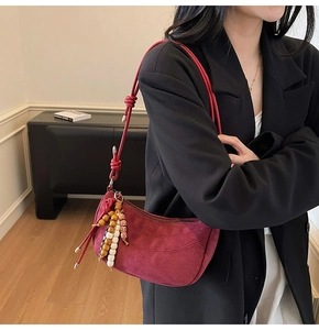 Detail of dark red suede crescent bag with knotted shoulder strap and beaded charms