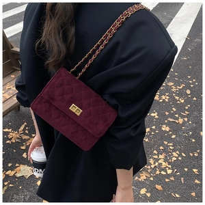 Detail of burgundy velvet crossbody bag with gold turn-lock and chain strap on street