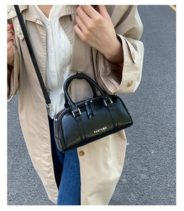 Vista de calle de un bolso Boston negro con logo PANTOR metálico sobre un abrigo beige