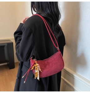 Detail of dark red suede croissant shoulder bag with vintage beaded charm and zipper closure