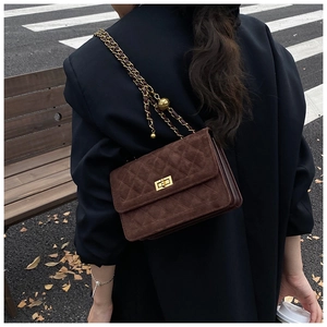 Brown suede crossbody bag with gold ball chain and quilted texture on a street background