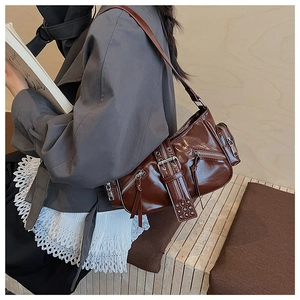 Detailed side view of dark brown glossy underarm bag with zippers and studs on shoulder