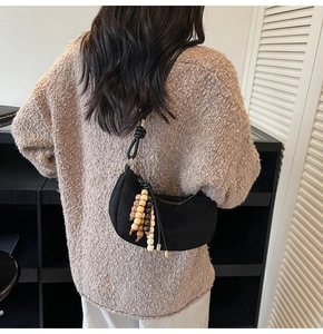 Close-up of a black crescent shoulder bag with colorful beaded charms on a beige sweater