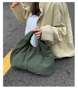 Close-up of a large dark green pleated tote bag held by a model on a gray road