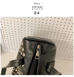 Close-up of black leather bag with silver rivets and metal zipper on white pegboard