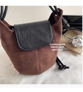 Détail d'un sac seau rétro en daim marron avec rabat en cuir noir sur un tissu blanc