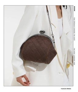 Detail of vintage brown quilted suede handbag with metal chain strap on white blazer
