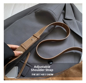 Detail of the adjustable brown leather shoulder strap with metallic buckle on a suede bag