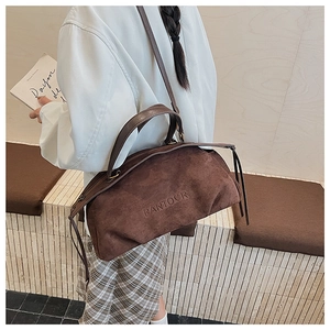 Detail of dark brown suede crossbody bag with embossed logo worn by a model