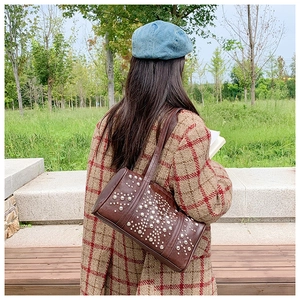 Deep brown cylindrical shoulder bag with silver rivet studs shown on a plaid coat