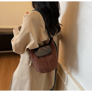 Sac seau chic en daim marron avec rabat en cuir noir porté sur un trench-coat kaki