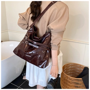 Side view of a glossy deep burgundy tote bag worn by a model in a minimalist room