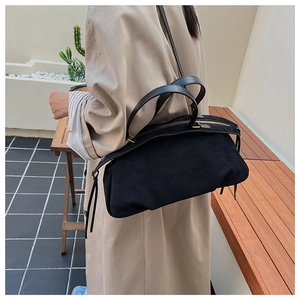 Detail of black suede Boston bag with embossed logo and tassel zipper on leather shoulder strap