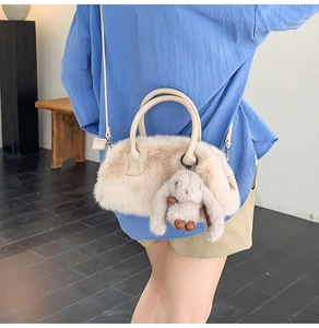 Dettaglio della borsa Boston in peluche beige con ciondolo a coniglio sul modello
