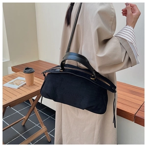 Close-up of black suede tote bag with fringe zip and embossed logo on light coat