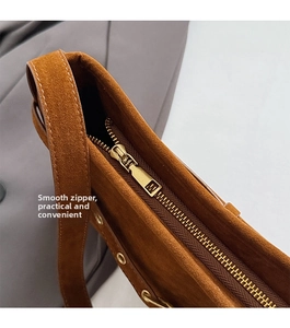 Close-up of smooth metal zipper and gold ring studs on brown matte leather tote bag