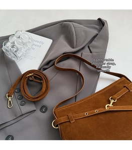 Detail of a brown suede crossbody bag with gold metal buckle and vintage strap on a grey suit