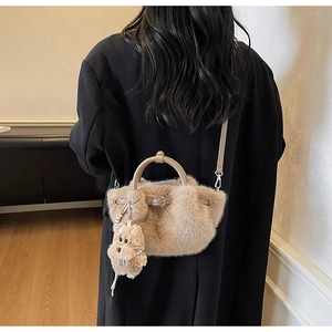 Plush beige bucket bag with teddy charm worn crossbody over a black blazer jacket