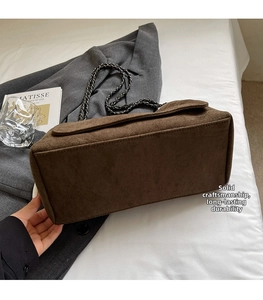Detail der braunen Wildleder-Schultertasche mit schwarzer Metallkette auf neutralem Grund