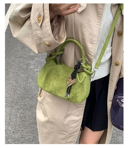 Detail of green suede handbag with twisted handle and heart charm shown on model