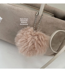 Nahaufnahme eines beigen Kunstfell-Pompons mit Silberkette an einer passenden Samthandtasche