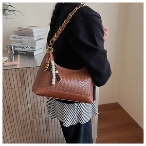 Détail du sac hobo tressé marron avec bandoulière chaîne dorée et gland en bois