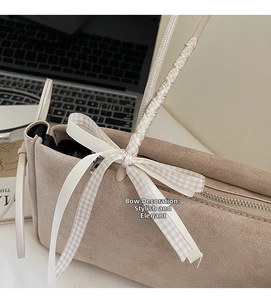 Detail der beigen Wildledertasche mit geflochtenem Griff und karierter Schleife