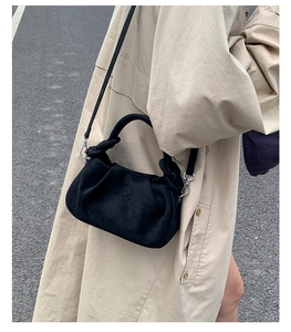 Close-up of matte black pleated cloud bag with silver hardware on beige trench coat