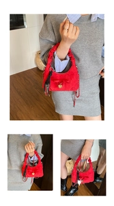 Detail of red faux suede crescent bag featuring pleated handle and gold heart charm