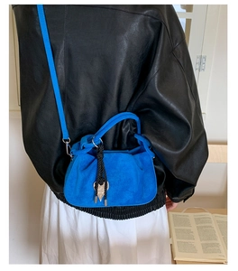 Detail view of a bright blue suede dumpling bag with black fringe tassel and metal cones