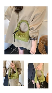 Close-up of green suede crescent bag featuring pleated handle and bow ornament
