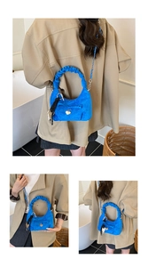 Detail of bright blue suede crescent bag with ruffled handle and heart charm decoration