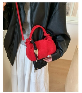 Detail of red suede bucket bag featuring woven knot charm and heart metal buckle