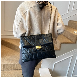 Close-up of black quilted shoulder bag with gold chain strap worn by a model