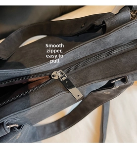 Detail of smooth metal zipper closure and wide shoulder strap on dark grey suede tote bag
